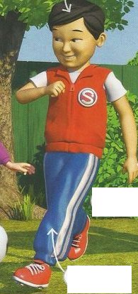 A boy in a red jacket and blue trousers walking and kicking a football
