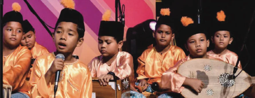 Murid memakai baju oren menyanyi dan bermain alat ghazal