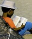 A boy sitting on a rock reading an open book