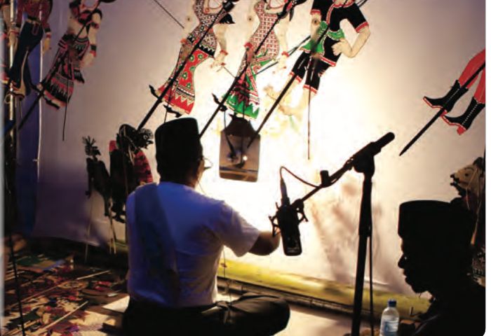 Tok dalang memainkan watak wayang kulit di hadapan layar yang diterangi cahaya