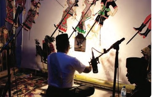 A puppeteer with flat puppets in front of a lit screen