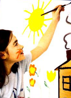 A girl with long brown hair painting a sun, flowers and a house on a wall