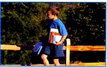 A boy with books walking beside a wooden fence