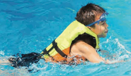 A boy swimming in a pool wearing a yellow life jacket