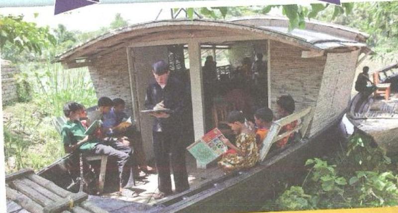 A teacher stands on a boat while children sit around him reading books
