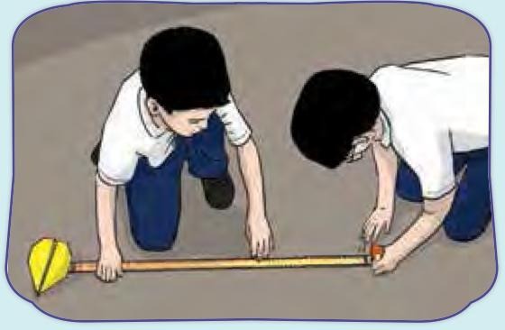 Dua murid mengukur jarak terbang kapal terbang kertas di lantai dengan pita pengukur