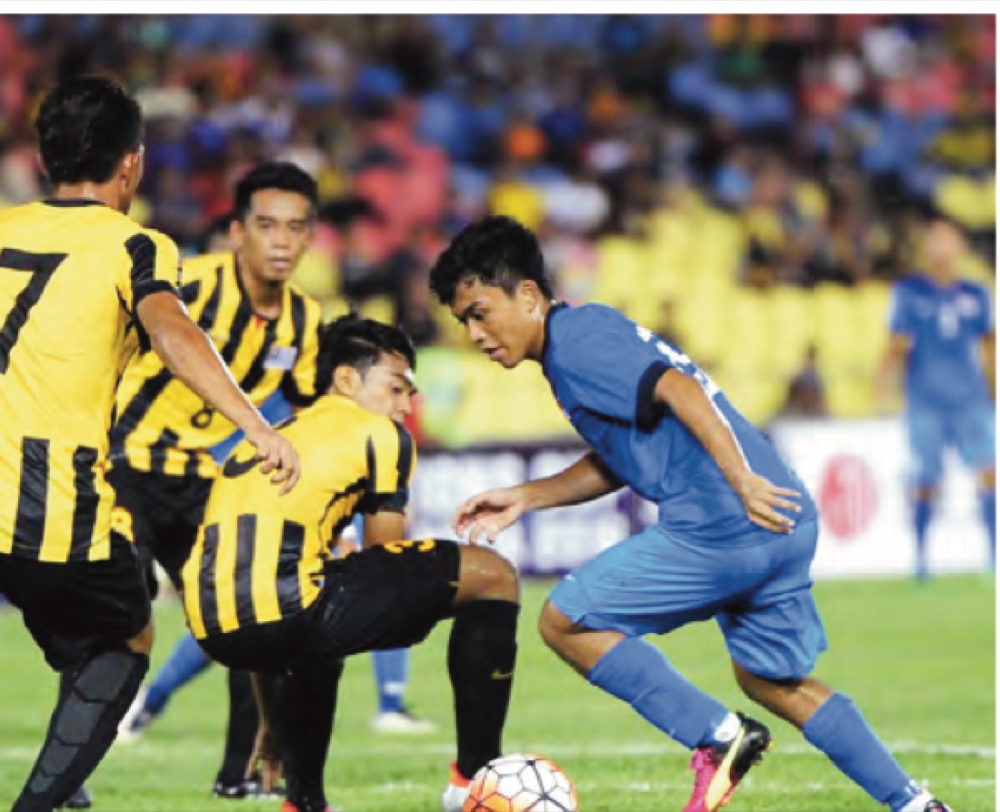 Pemain bola sepak berbaju kuning dan hitam berlari merebut bola dengan pemain berbaju biru