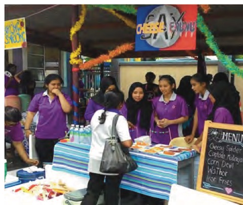Murid berbaju ungu menjaga gerai jualan makanan yang berhias pada Hari Keusahawanan