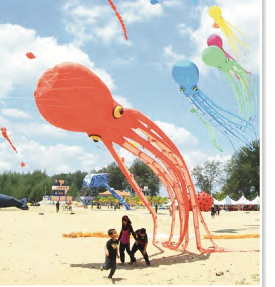 Layang-layang besar berbentuk sotong terbang di atas pantai dan kanak-kanak berlari