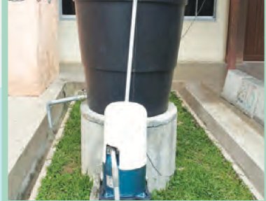 Pam dan paip telaga tiub di sebelah tangki air di halaman rumah