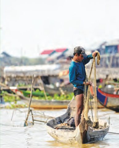 Seorang nelayan berdiri di atas perahu sambil memegang jala di sebuah tasik
