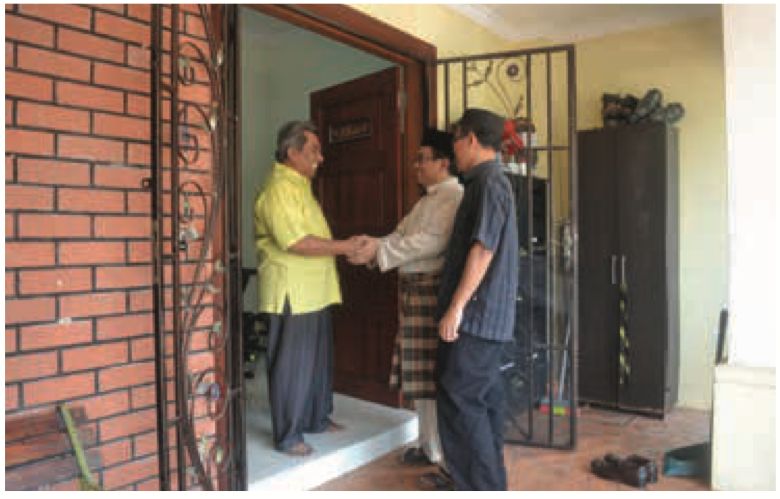 Tiga lelaki berjabat tangan di pintu rumah