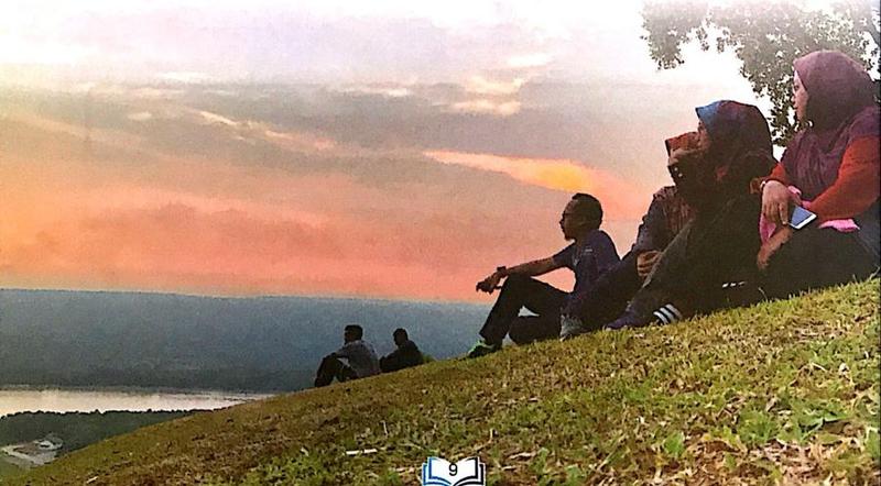 Sekumpulan remaja duduk di bukit memerhati matahari terbenam
