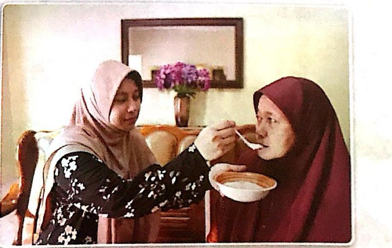 Seorang anak perempuan menyuap bubur kepada ibunya yang sakit