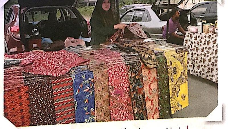 Seorang peniaga wanita menyusun kain batik di gerai tepi jalan
